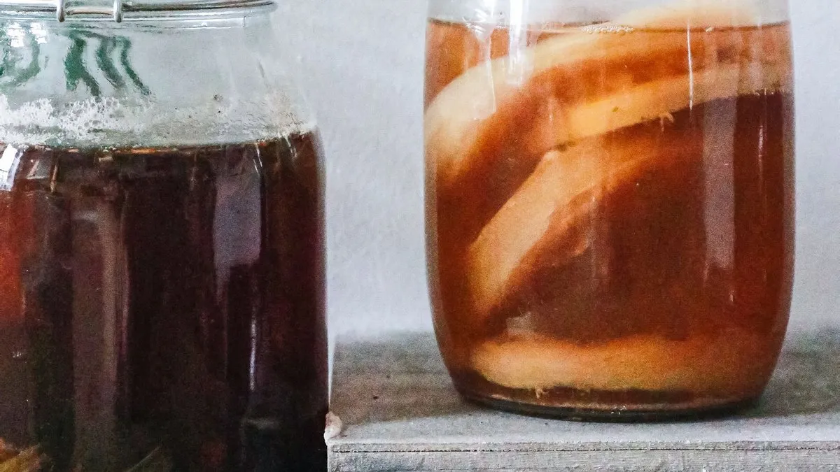 Bocaux de kombucha maison en fermentation avec la mère de kombucha visible, couverts d'un tissu