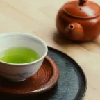 Bol de thé vert à la robe vert vif et théière japonaise en terre rouge sur une table en bois clair