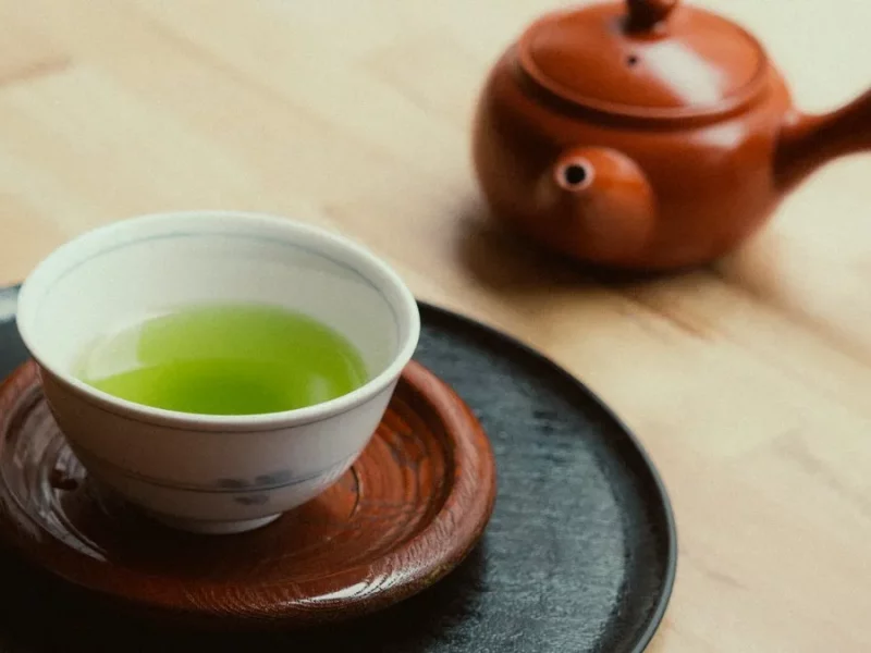 Bol de thé vert à la robe vert vif et théière japonaise en terre rouge sur une table en bois clair