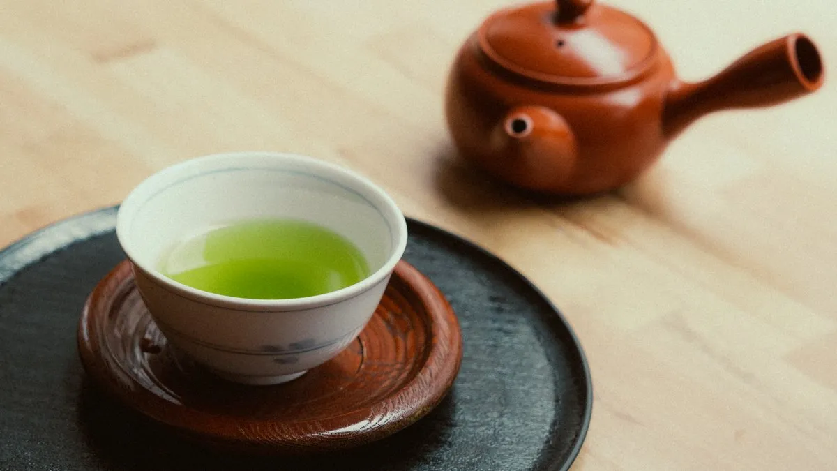 Bol de thé vert à la robe vert vif et théière japonaise en terre rouge sur une table en bois clair