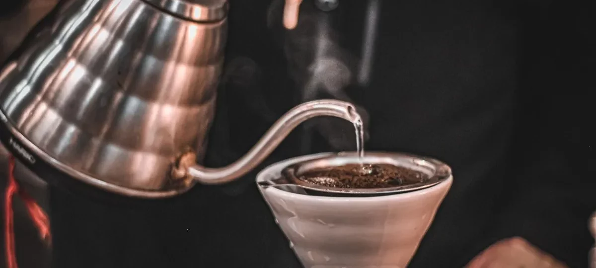 Bouilloire col de cygne en inox versant un filet d'eau chaude sur le café moulu d'un dripper