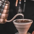 Bouilloire col de cygne en inox versant un filet d'eau chaude sur le café moulu d'un dripper