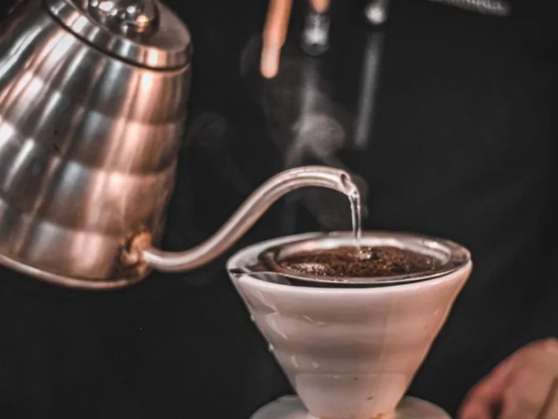 Bouilloire col de cygne en inox versant un filet d'eau chaude sur le café moulu d'un dripper