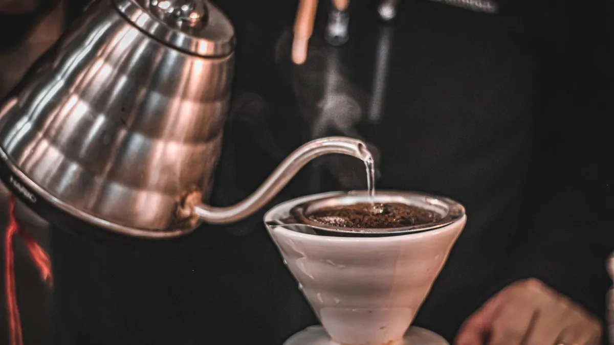 Bouilloire col de cygne en inox versant un filet d'eau chaude sur le café moulu d'un dripper