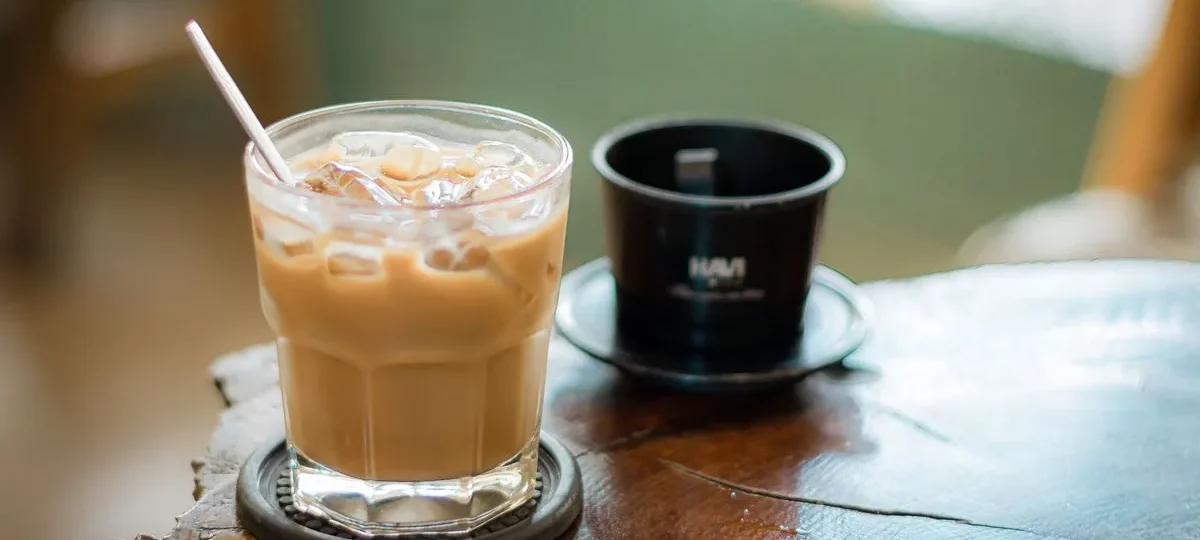 Café glacé vietnamien au lait concentré dans un verre, à côté d'un filtre phin en métal