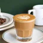 Café noisette dans un petit verre sur soucoupe, pot à lait et grains de café sur une table de café