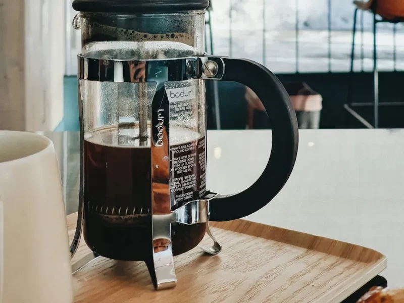 Cafetière à piston Bodum en verre remplie de café, posée sur un plateau en bois près d'une baie vitrée