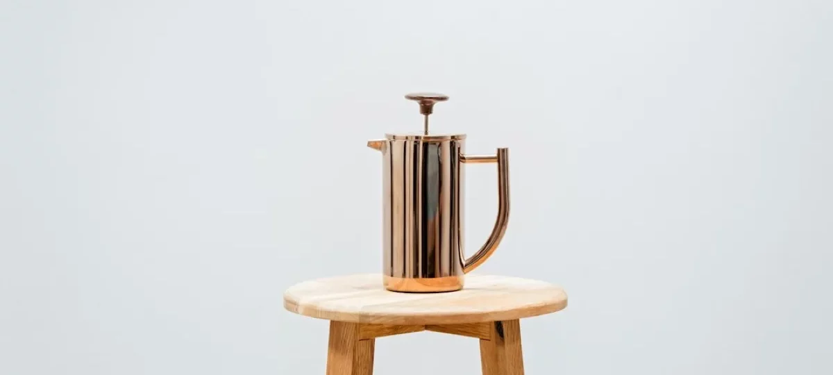 Cafetière à piston inox double paroi posée sur un tabouret en bois, fond clair