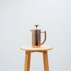 Cafetière à piston inox double paroi posée sur un tabouret en bois, fond clair