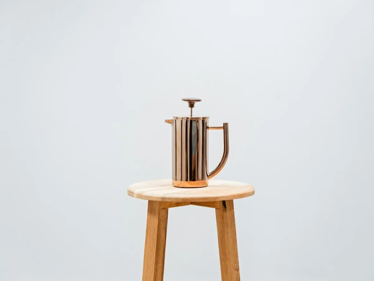 Cafetière à piston inox double paroi posée sur un tabouret en bois, fond clair