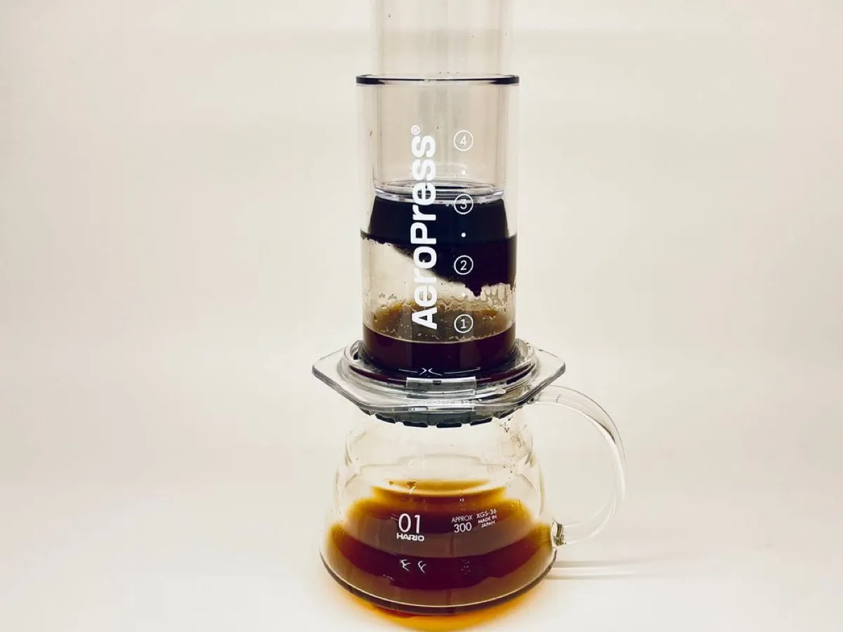 Cafetière Aeropress transparente posée sur une carafe en verre, café en immersion et café filtré en dessous
