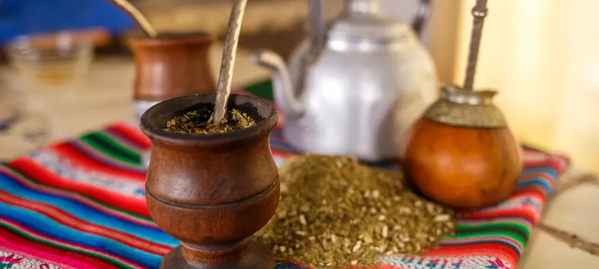 Calebasses de maté remplies de yerba avec leur bombilla, yerba en vrac et bouilloire sur un tissu andin