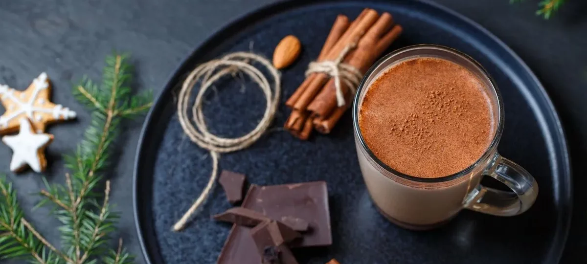 Chocolat chaud maison dans une tasse en verre, avec carrés de chocolat noir et bâtons de cannelle