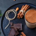 Chocolat chaud maison dans une tasse en verre, avec carrés de chocolat noir et bâtons de cannelle