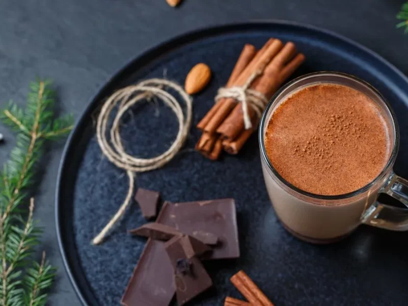 Chocolat chaud maison dans une tasse en verre, avec carrés de chocolat noir et bâtons de cannelle