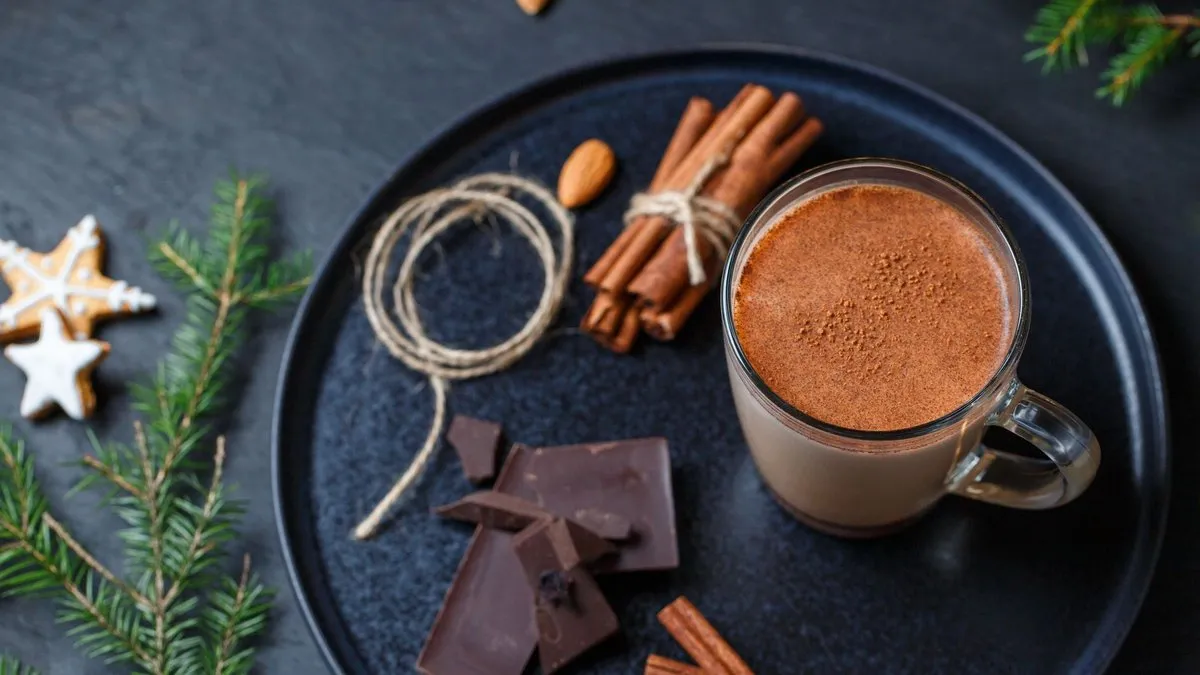 Chocolat chaud maison dans une tasse en verre, avec carrés de chocolat noir et bâtons de cannelle