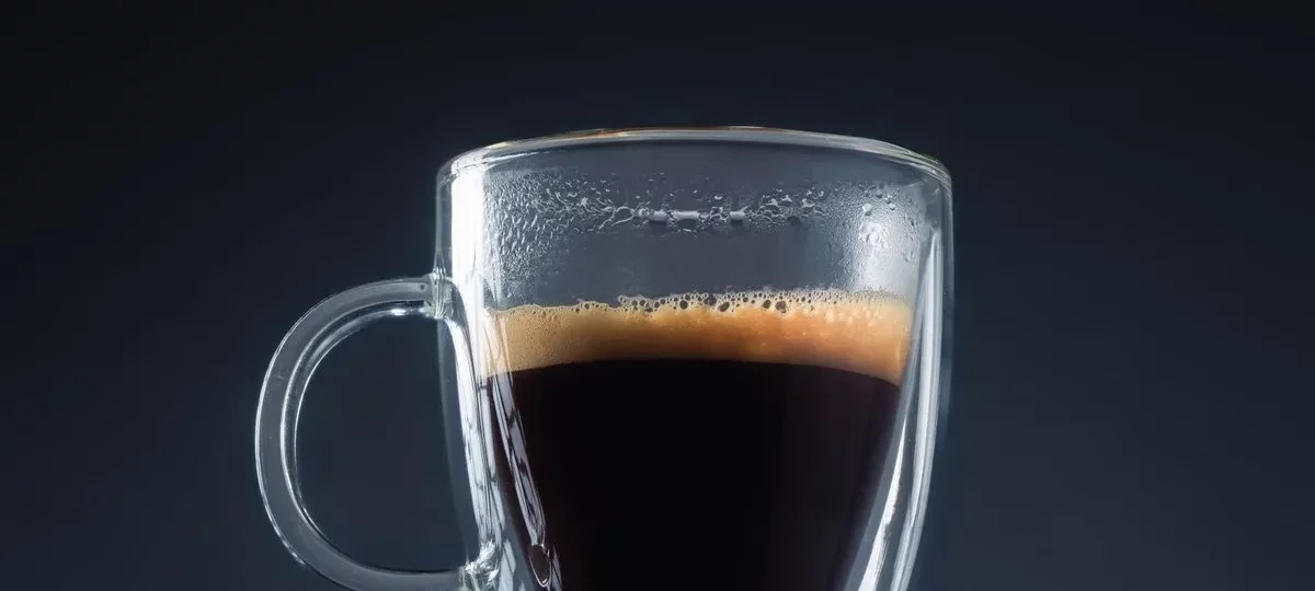 Doppio, double expresso à la crema dorée dans une tasse en verre sur fond sombre
