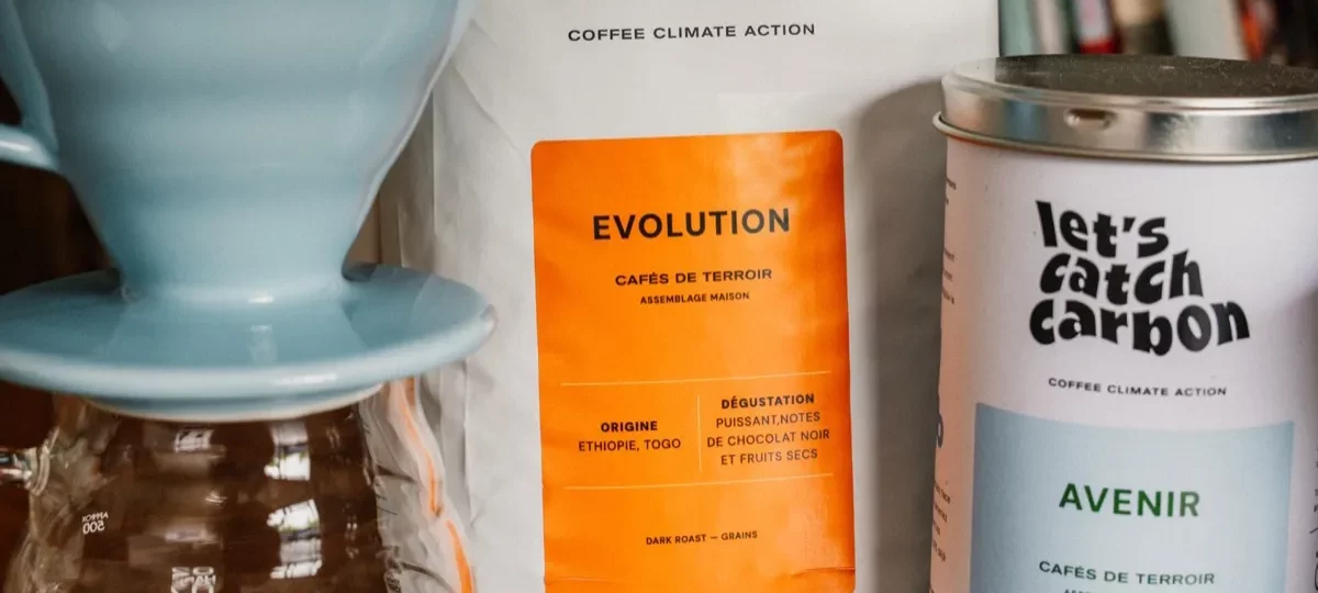 Dripper Hario V60 bleu posé sur une carafe en verre, avec un sachet et une boîte de café en grains
