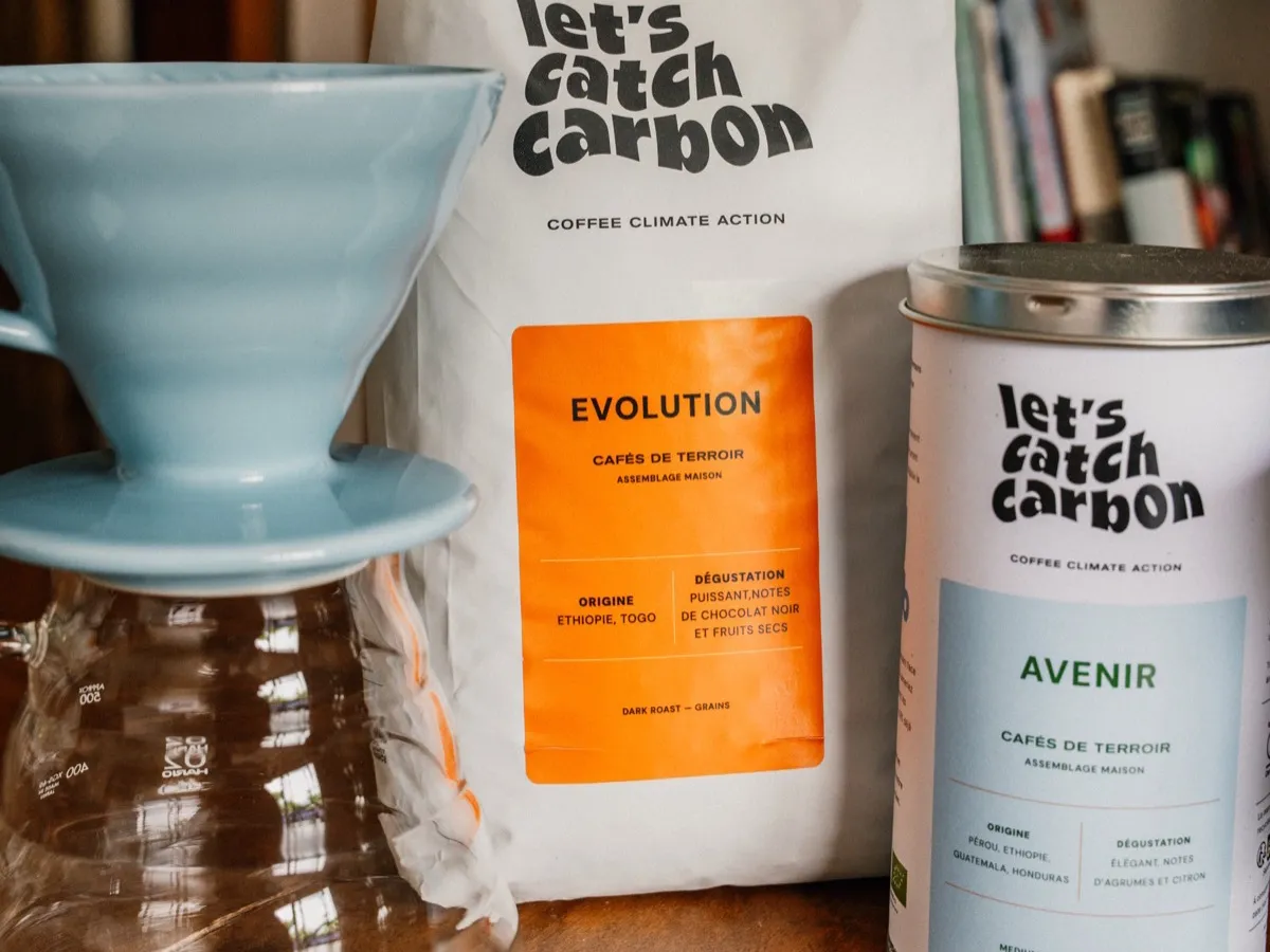 Dripper Hario V60 bleu posé sur une carafe en verre, avec un sachet et une boîte de café en grains
