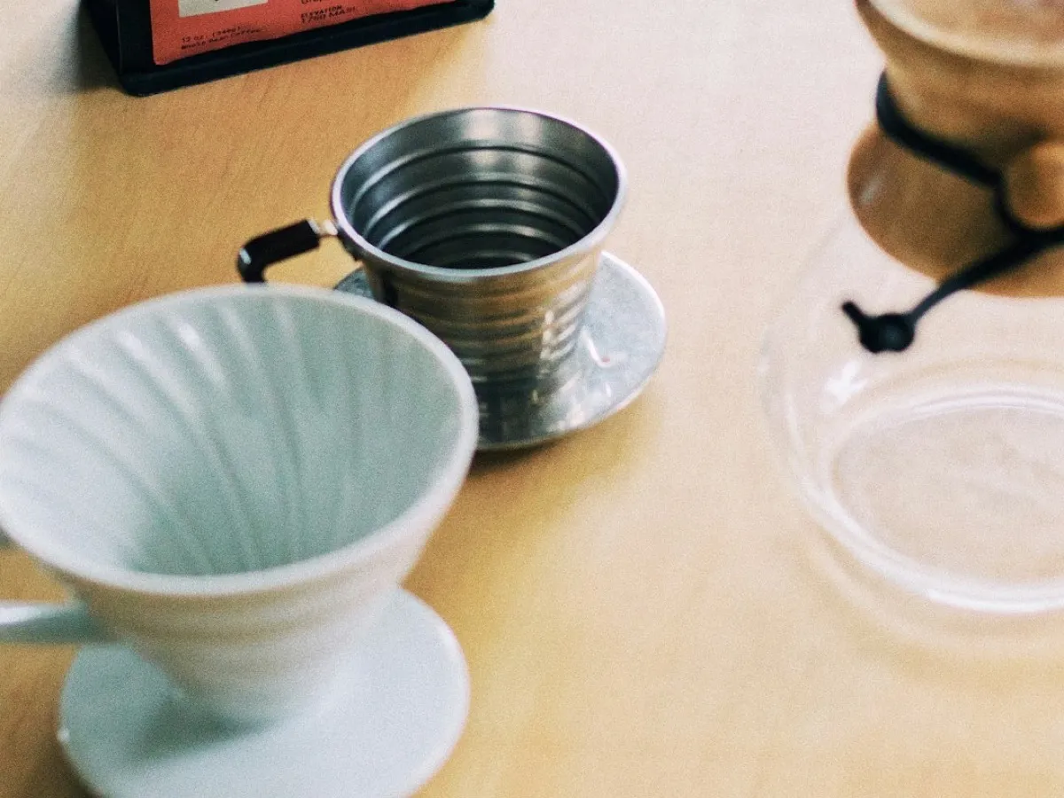 Dripper Hario V60 en céramique blanche, dripper Kalita en inox et cafetière Chemex sur une table en bois clair