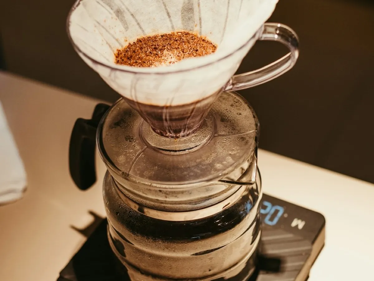 Dripper V60 en verre avec filtre papier et café moulu, posé sur une carafe et une balance de précision