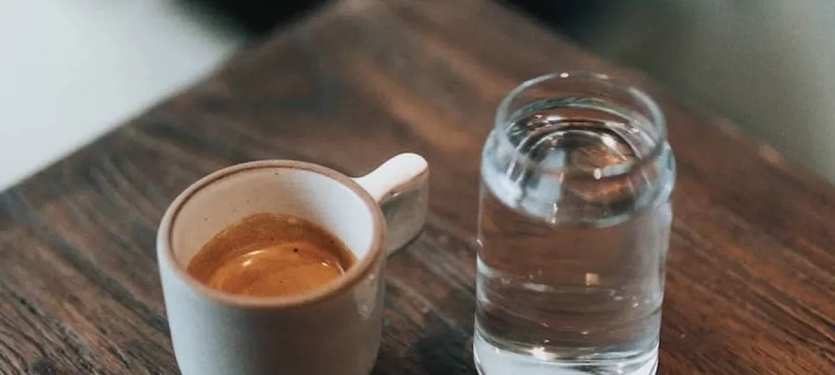 Espresso et verre d'eau posés sur une table en bois, l'eau étant à l'origine du calcaire