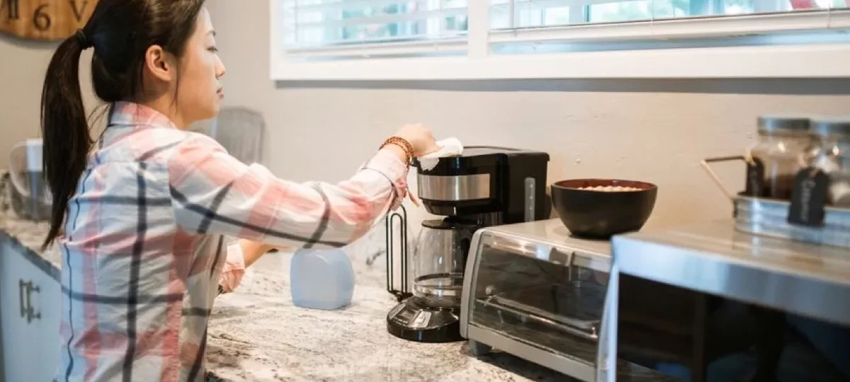Femme nettoyant une cafetière dans une cuisine lumineuse, geste d'entretien qui précède le détartrage