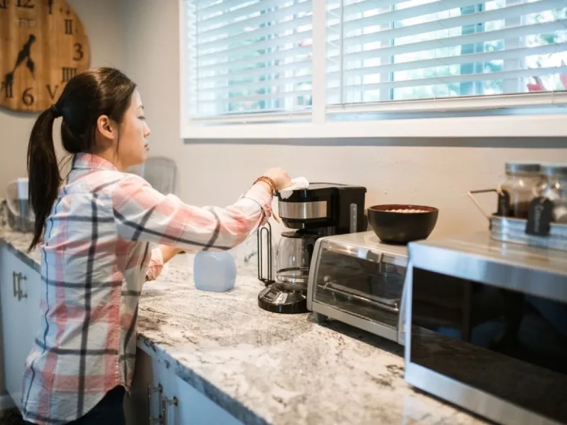 Femme nettoyant une cafetière dans une cuisine lumineuse, geste d'entretien qui précède le détartrage