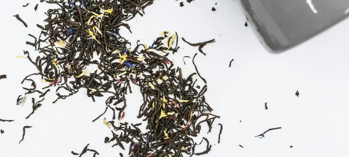 Feuilles de thé Earl Grey en vrac aux pétales de bleuet versées d'un sachet vers une tasse