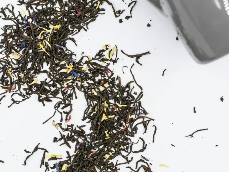 Feuilles de thé Earl Grey en vrac aux pétales de bleuet versées d'un sachet vers une tasse