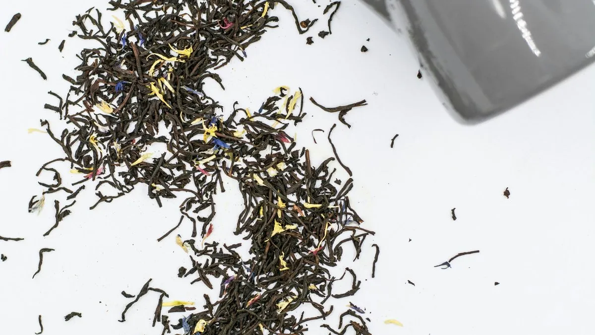 Feuilles de thé Earl Grey en vrac aux pétales de bleuet versées d'un sachet vers une tasse