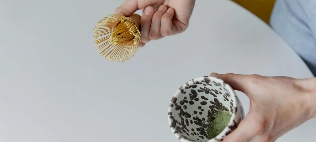 Fouet chasen en bambou tenu au-dessus d'un bol de matcha en cours de préparation