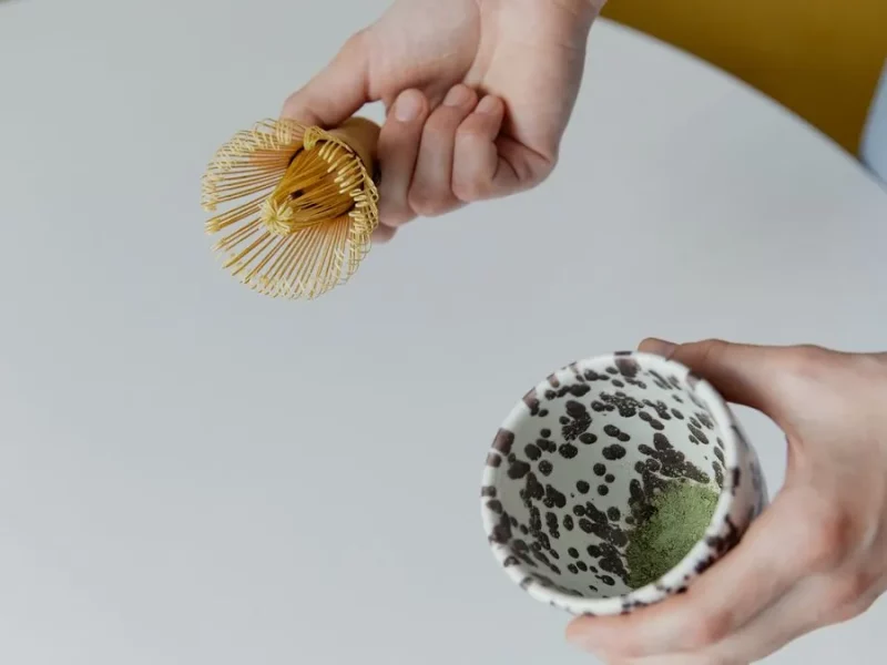 Fouet chasen en bambou tenu au-dessus d'un bol de matcha en cours de préparation