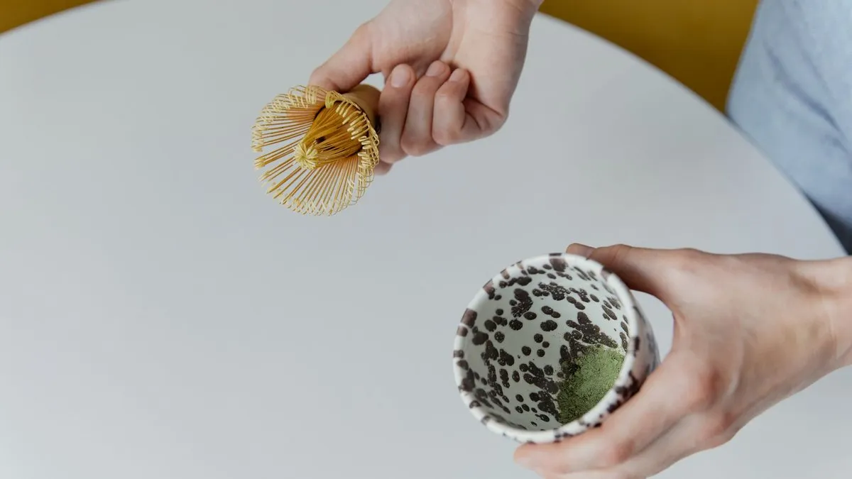 Fouet chasen en bambou tenu au-dessus d'un bol de matcha en cours de préparation