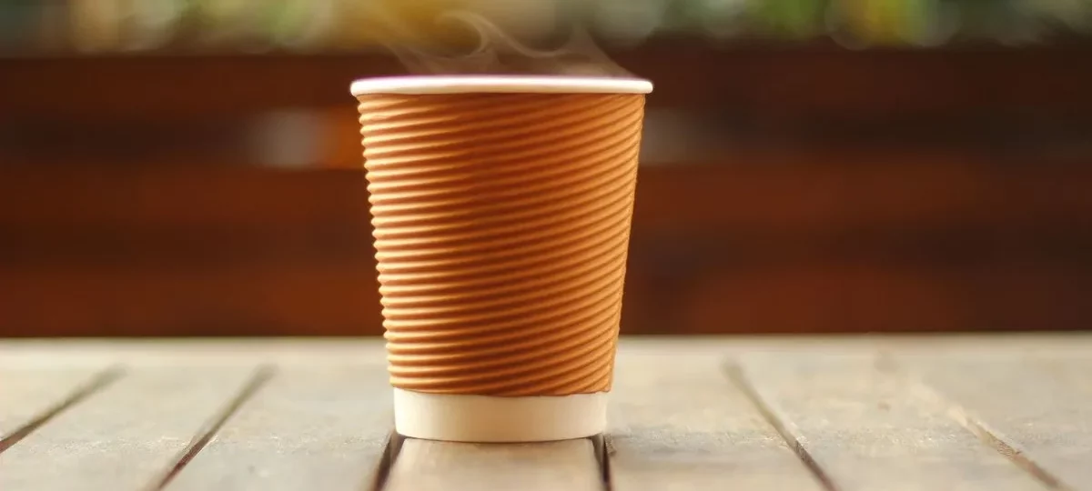 Gobelet de café chaud fumant posé sur une table en bois