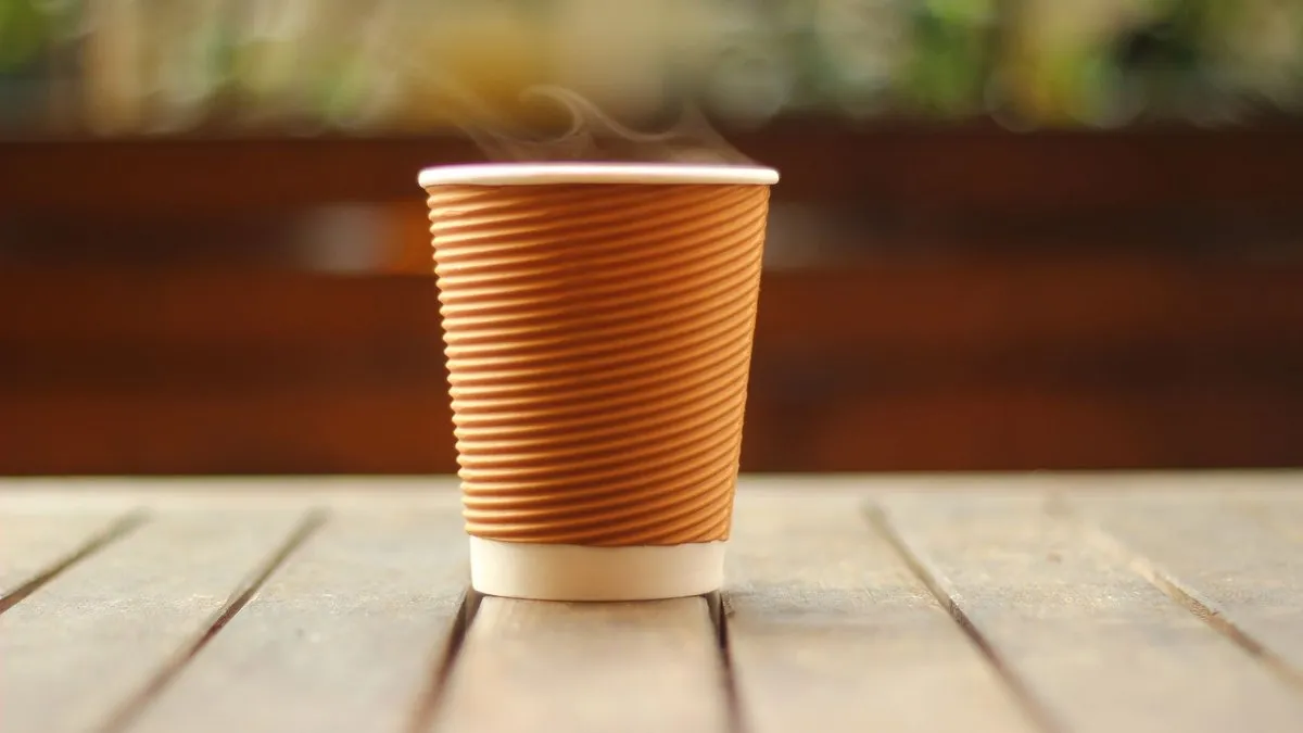 Gobelet de café chaud fumant posé sur une table en bois
