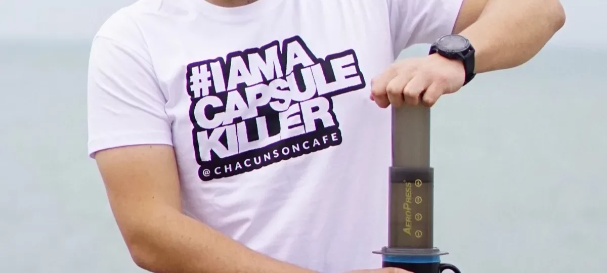 Homme pressant le piston d'une cafetière Aeropress posée sur un mug, au bord de mer