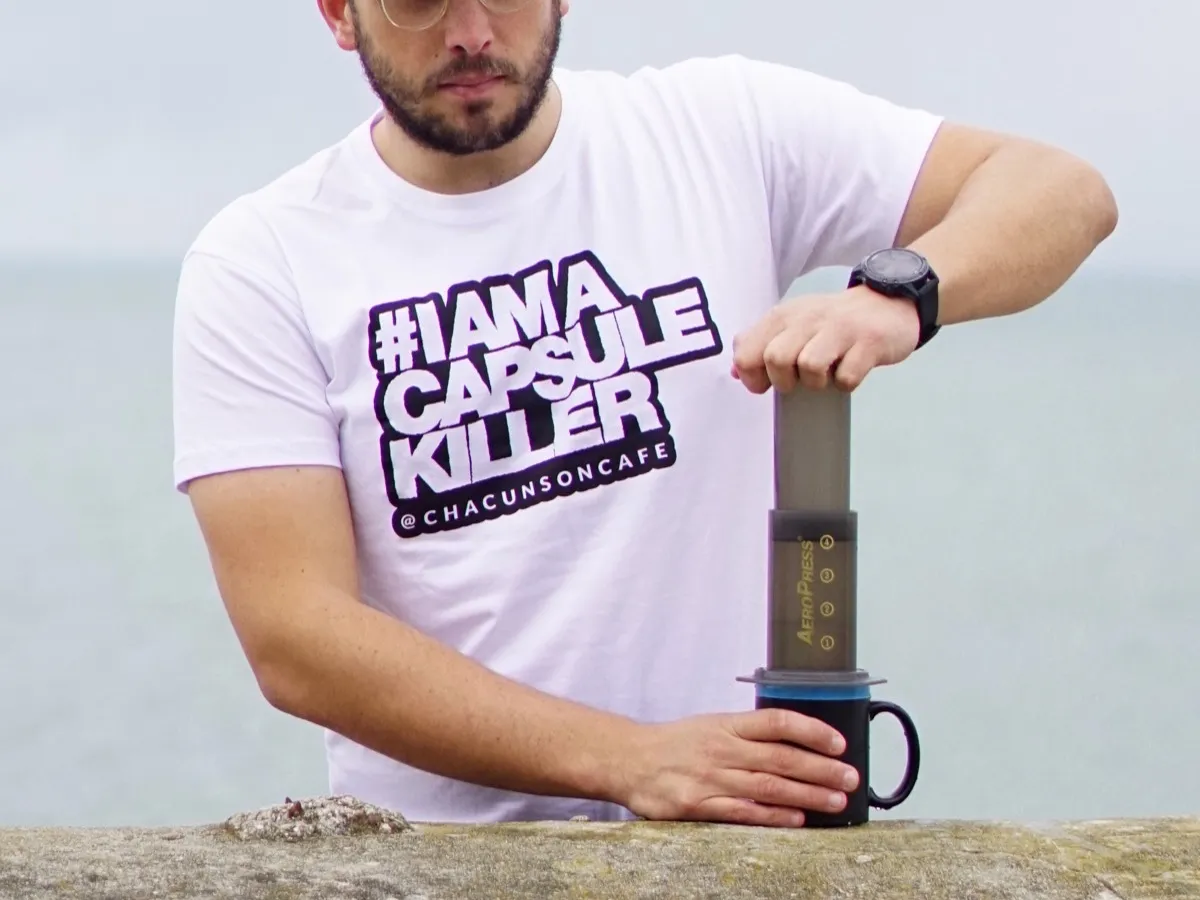 Homme pressant le piston d'une cafetière Aeropress posée sur un mug, au bord de mer