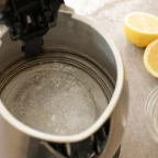 Intérieur d'une bouilloire inox couvert de calcaire, à côté d'un citron coupé et d'un bol de vinaigre blanc