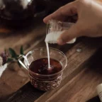 Lait versé dans une tasse en verre de thé noir, théière en verre en arrière-plan sur table en bois