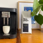 Machine à café à grains De'Longhi Magnifica Evo avec tasse sous la buse, à côté d'un sachet de café en grains