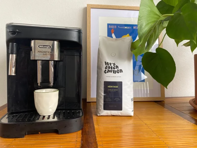 Machine à café à grains De'Longhi Magnifica Evo avec tasse sous la buse, à côté d'un sachet de café en grains