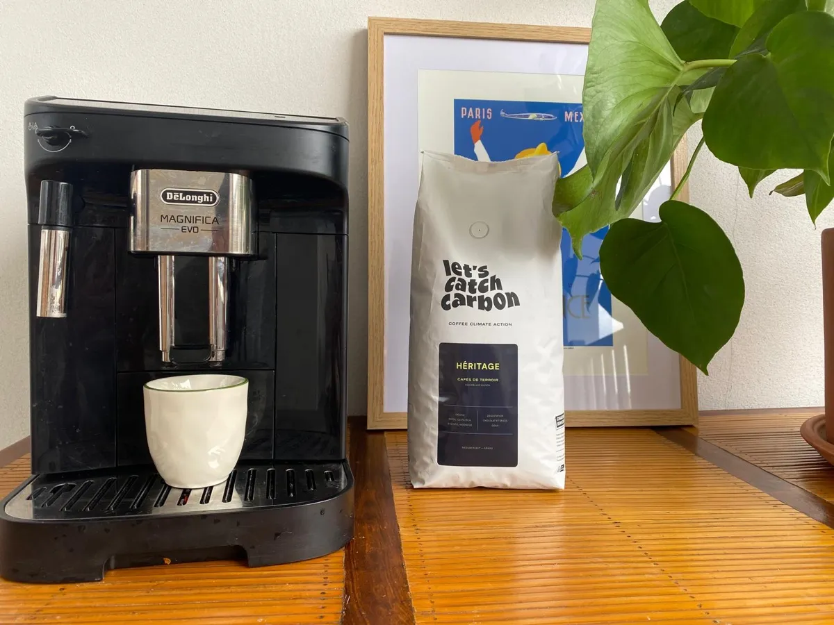 Machine à café à grains De'Longhi Magnifica Evo avec tasse sous la buse, à côté d'un sachet de café en grains
