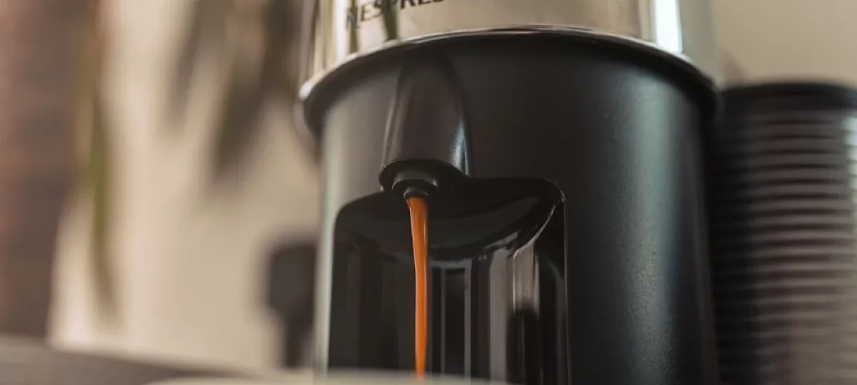 Machine Nespresso Vertuo chromée versant un café dans une tasse blanche, avant son détartrage