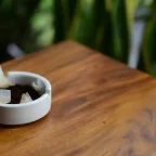 Marc de café usagé dans une petite coupelle blanche sur une table en bois, plantes vertes derrière