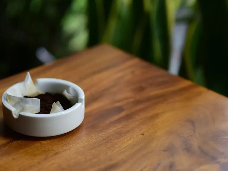 Marc de café usagé dans une petite coupelle blanche sur une table en bois, plantes vertes derrière