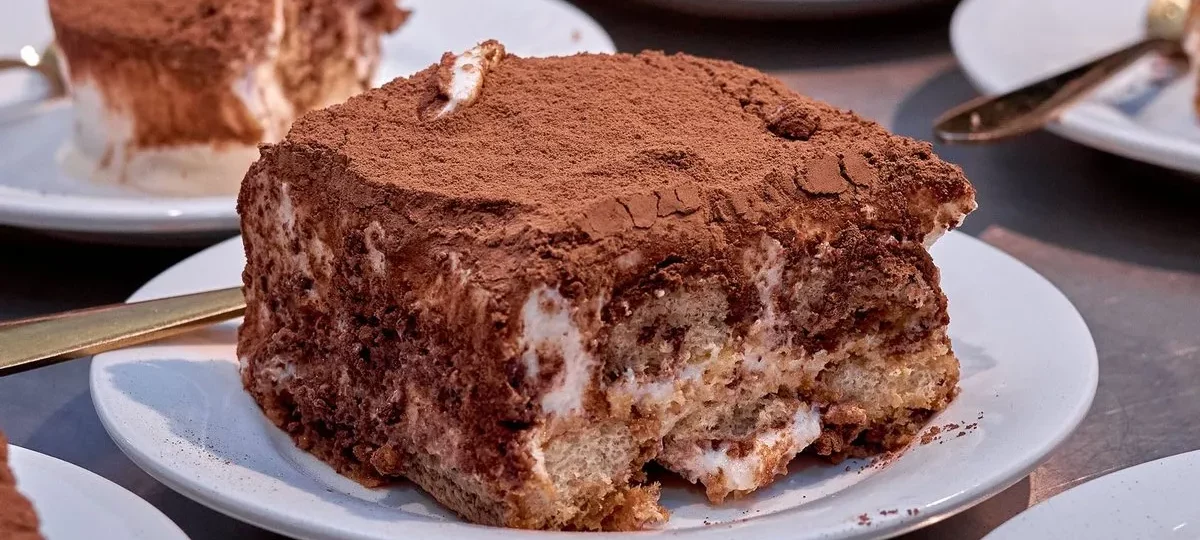 Parts de tiramisu aux biscuits nappées de cacao servies sur des assiettes à dessert