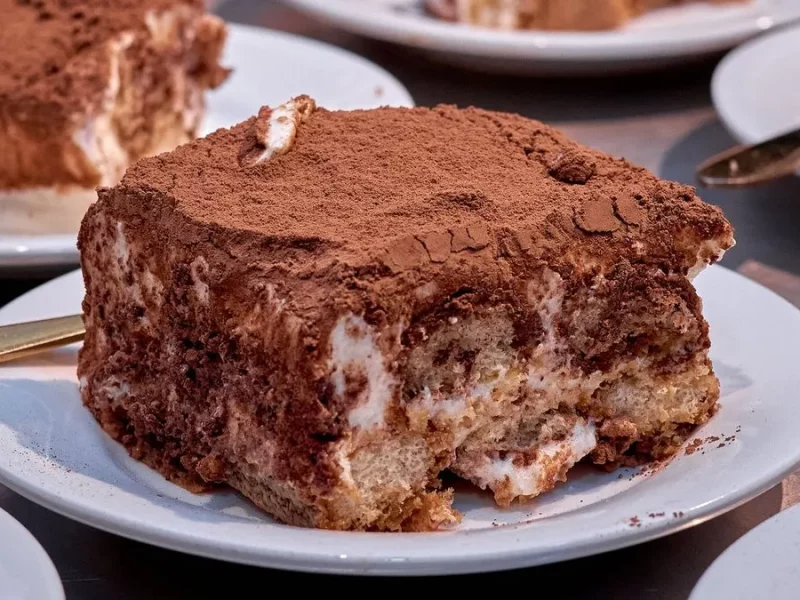 Parts de tiramisu aux biscuits nappées de cacao servies sur des assiettes à dessert