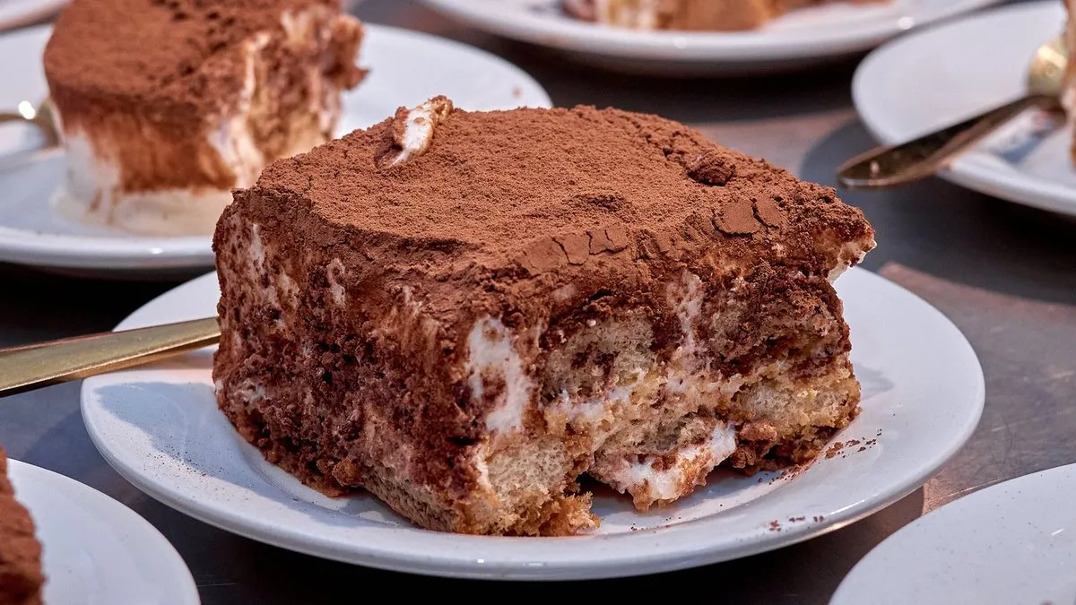 Parts de tiramisu aux biscuits nappées de cacao servies sur des assiettes à dessert