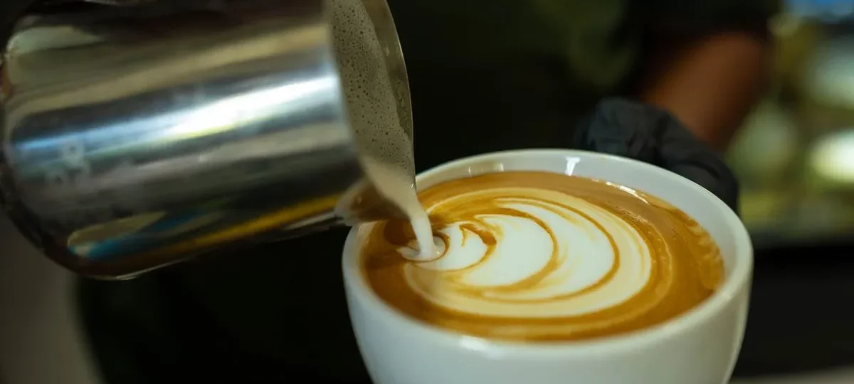 Pichet à lait en inox dessinant une rosace de latte art dans une tasse de café